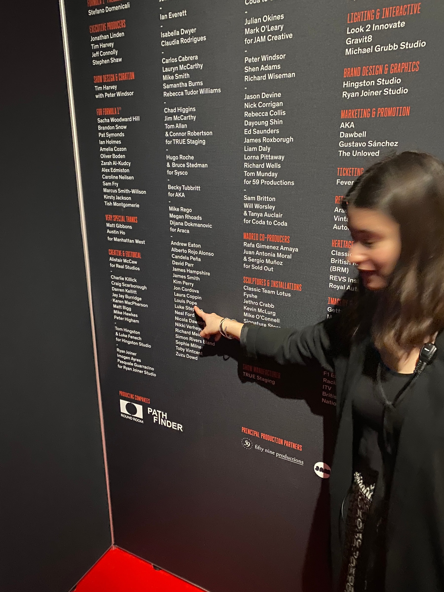 A finger pointing to a name on the exhibition credits wall