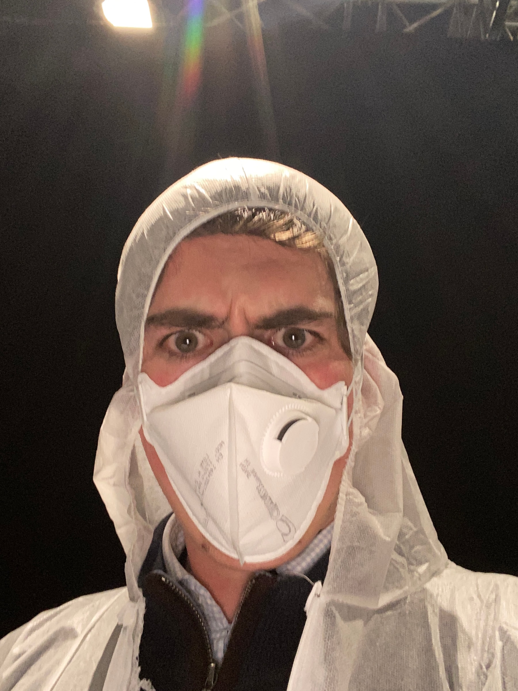 Louis in a white protective suit and mask under set lighting