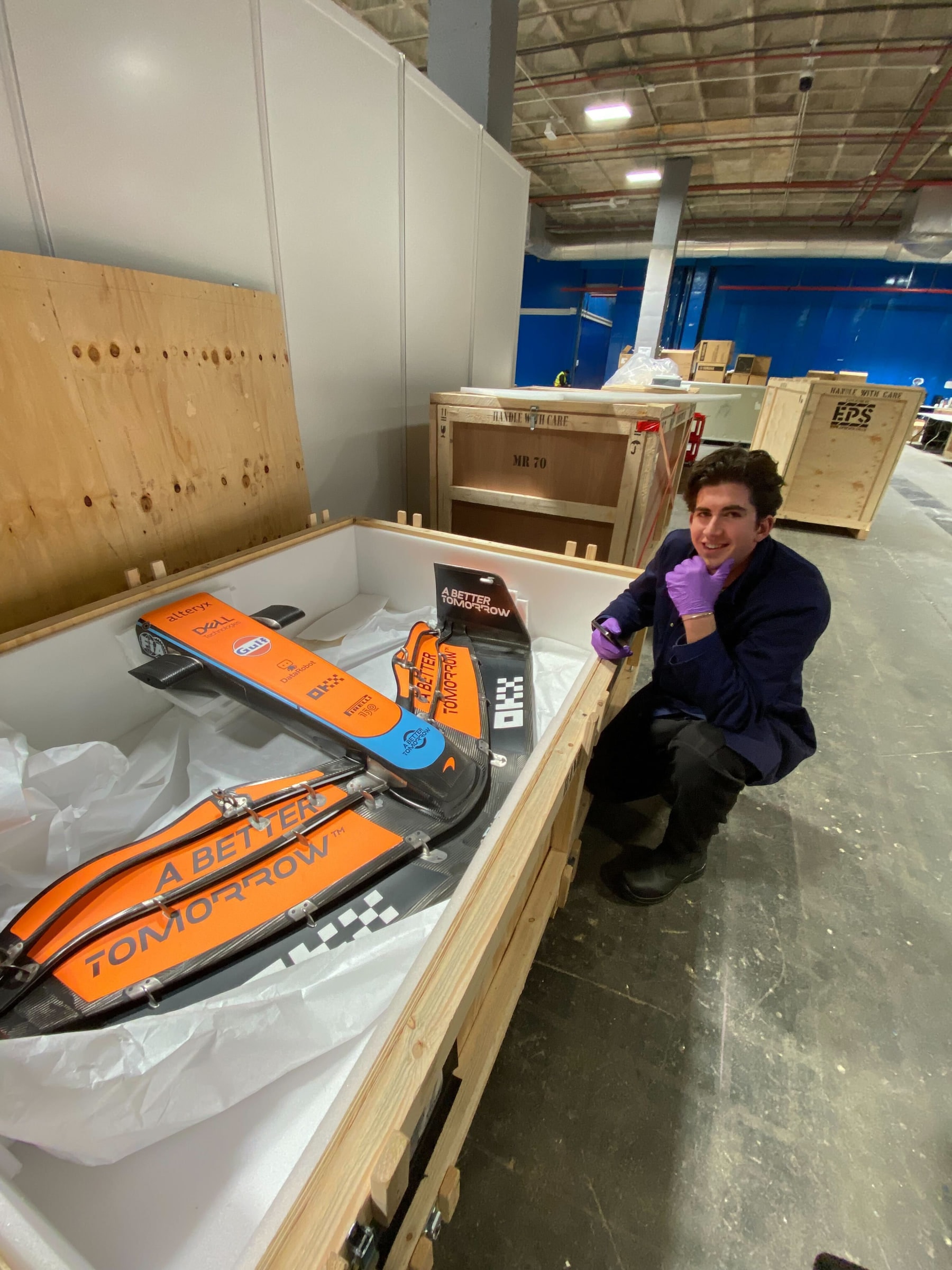 Louis kneeling beside a McLaren front wing packed in a custom crate