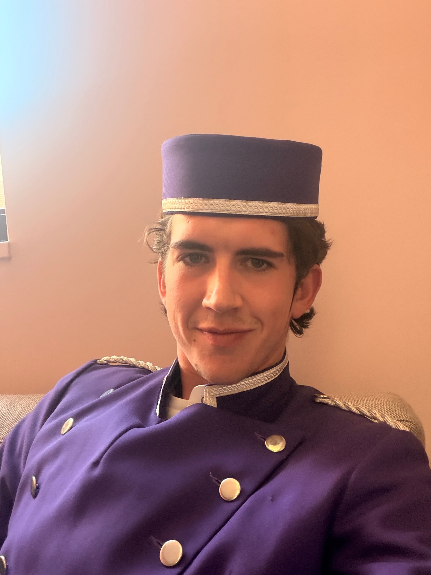 Louis in a purple bellhop uniform and pillbox hat on a period set