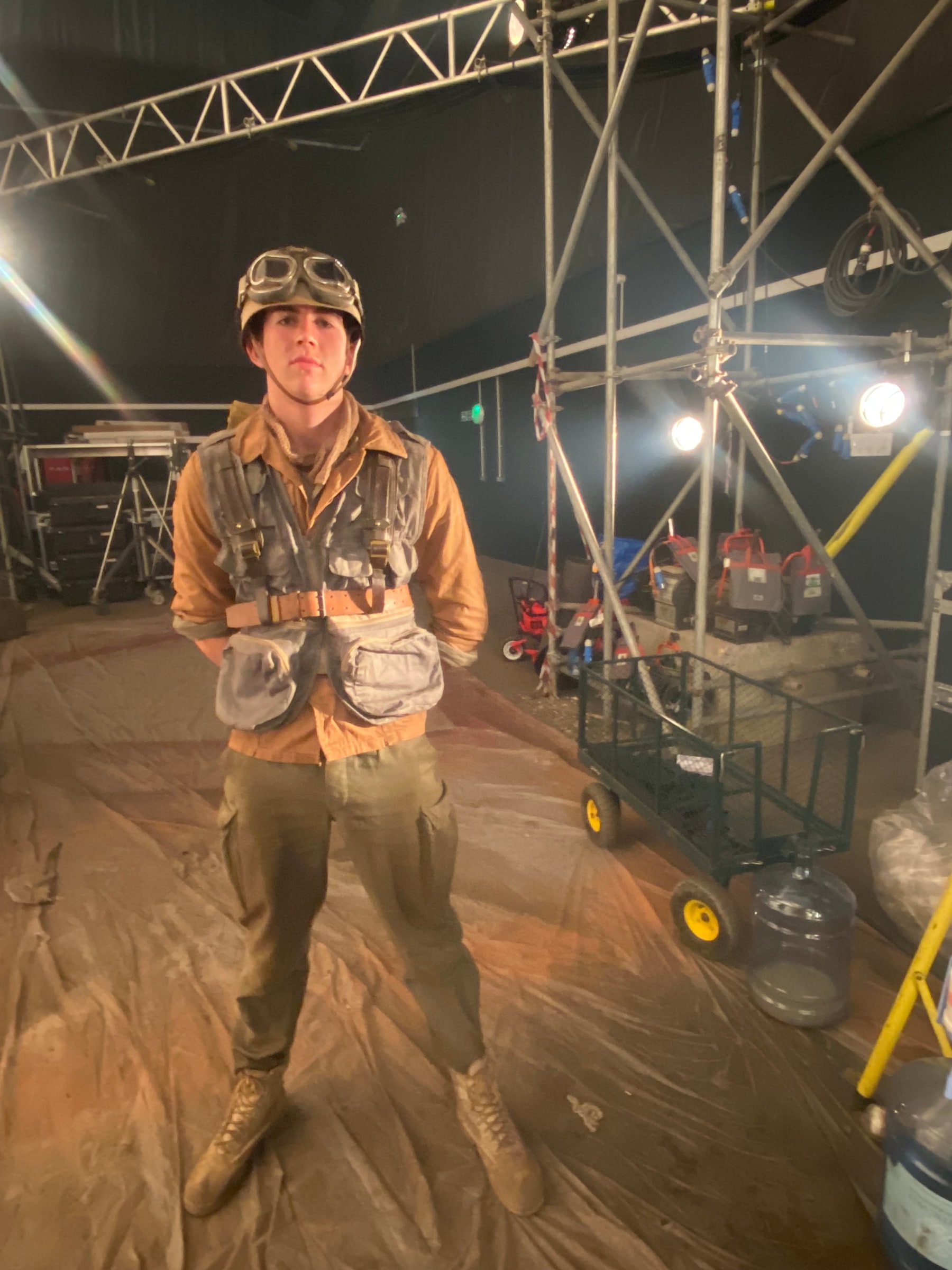 Louis in a 1940s flight jacket and goggles on a dressed film set