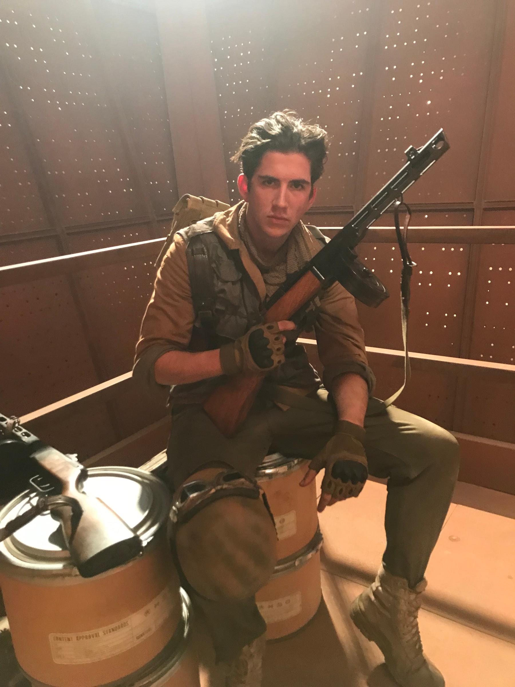 Louis in costume with a prop rifle, sitting on set between takes